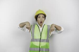 A shocked Asian woman labor wearing safety helmet and vest, pointing to copy space below her, isolated by white background. Labor's day concept. photo