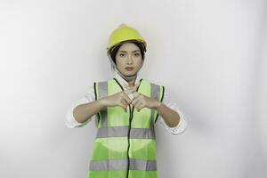 hermosa asiático mujer labor trabajador vistiendo un la seguridad casco y chaleco con mano gesticulando rechazo o prohibición aislado blanco antecedentes. mano de obra día concepto. foto