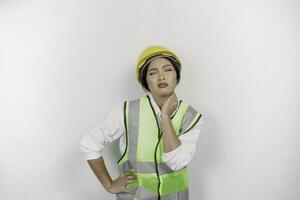 Tired Asian woman labor worker wearing a safety helmet and vest suffering from pain, muscle spasm isolated white background. Labor's day concept. photo