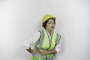 asiático mujer labor trabajador vistiendo un la seguridad casco y chaleco sostener mano en estómago sufre dolor aislado blanco antecedentes. mano de obra día concepto. foto