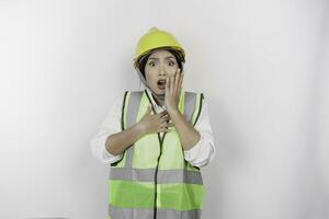 un retrato de un conmocionado asiático mujer labor vistiendo la seguridad casco y chaleco mientras su boca amplio abierto, aislado por blanco antecedentes. mano de obra día concepto foto