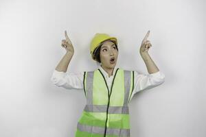 un conmocionado asiático mujer labor vistiendo la seguridad casco y chaleco, señalando a Copiar espacio encima su, aislado por blanco antecedentes. mano de obra día concepto. foto
