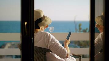 Woman with wine glass using cell when relaxing at the balcony overlooking sea video