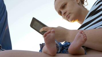 mamma con addormentato bambino a il spiaggia donna utilizzando cellulare video