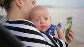 Mother with baby video chatting on cellphone at the beach