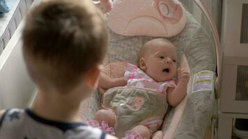 Brother rocking baby sister in chair at home video