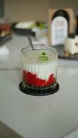 A glass of strawberry drink with milk and mint leaf topping on a white table in a cafe. photo