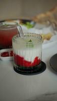 A glass of strawberry drink with milk and mint leaf topping on a white table in a cafe. photo