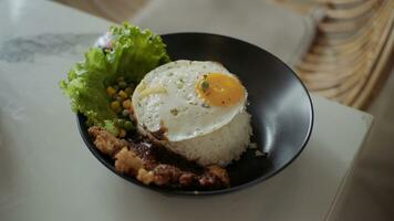 arroz cuenco con soleado lado arriba huevo, pollo, vegetales y lechuga en blanco mesa en restaurante. foto