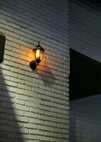 clásico pared lámpara en blanco ladrillo a noche. estético naranja calle Encendiendo. foto