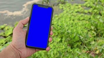 Hand halten Handy, Mobiltelefon Telefon Blau Bildschirm auf verwischen Natur Hintergrund video