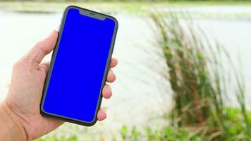 hand- Holding mobiel telefoon blauw scherm Aan vervagen natuur achtergrond video