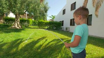 Child taking part in household duties and watering green lawn by the house video