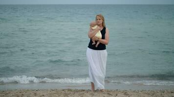 Mother with lost look holding baby being alone at the beach near sea video