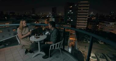 Man and woman having drinks on the rooftop cafe in night city video