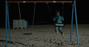 Kid swinging alone on the beach at night video