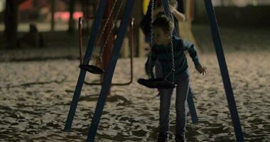 Kind haben Spaß mit leeren Schaukeln auf Spielplatz im das Abend video