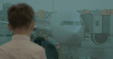 ragazzo in attesa a aeroporto e guardare a aereo attraverso il finestra video