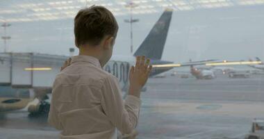 niño esperando para vuelo y mirando a aviones mediante el ventana video