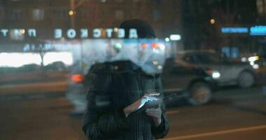 jong vrouw surfing internet Aan stootkussen wanneer aan het wachten voor bus in avond stad video