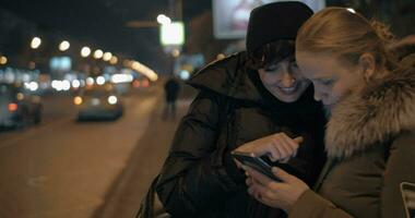 Dames aan het kijken iets Aan mobiel terwijl aan het wachten Bij bus hou op in de avond video