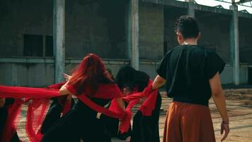 a group of Asian men are playing with red cloth ropes with their friends in a tug of war video