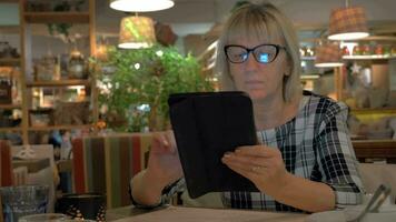Senior mulher surfar Internet em almofada dentro cafeteria video