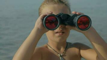 Slow motion view of small boy watching with binoculars against blurred sea video