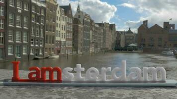 Aussicht von klein Plastik Zahl von ich bin Amsterdam Briefe Skulptur auf das Brücke gegen verschwommen Stadtbild, amsterdam, Niederlande video