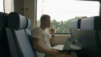 Visão do jovem homem equitação dentro a trem e trabalhando com computador portátil em a mesa contra janela, Países Baixos video