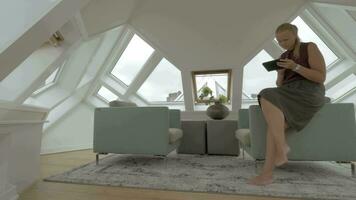 Visualizza di giovane biondo donna seduta su il lato di braccio sedie utilizzando tavoletta dentro di camera nel un' cubo Casa Rotterdam, Olanda video