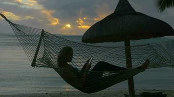 Woman with phone lying in hammock on the beach video