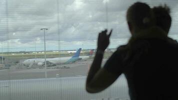 Back view of mother and son standing and watching in the window on the airplane runway, Amsterdam, Netherlands video