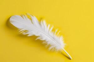 Close up of bright white feather. Copy space, yellow background. Fashion and Party concept. photo