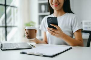 Asian Woman using smart phone for mobile payments online shopping, omni channel, sitting on table, virtual icons graphics interface screen photo