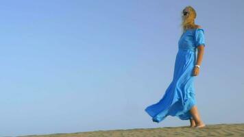 Slow motion view of young blond woman standing against blue sky in long blue dress and it is fluttering on the wind video