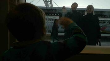 Slow motion view of boy watching in window from rail train and saying goodbye his grandparents, swinging arms video