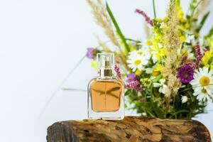 a perfume bottle on the background of a dry stump, tree bark and a bouquet of wild flowers. Stylish appearance, layout, personality. Banner, a place for the text. photo