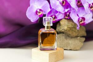 The perfume bottle stands on a wooden pedestal against a background of stone and beautiful orchids. Stylish appearance of the product, layout, personality. Banner, a place for the text. photo