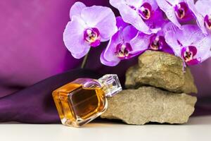 A perfume bottle stands on a stone against a background of beautiful orchids. Stylish appearance, layout, personality. Banner, a place for the text. photo