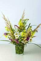 un ramo de flores de salvaje flores en un pequeño vaso florero en un blanco antecedentes. elegante apariencia, disposición, personalidad. bandera, un sitio para el texto foto