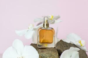 A perfume bottle stands on a stone against a background of beautiful orchids. Stylish appearance, layout, personality. Banner, a place for the text. photo