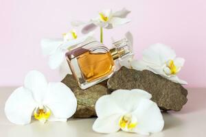 A perfume bottle stands on a stone against a background of beautiful orchids. Stylish appearance, layout, personality. Banner, a place for the text. photo