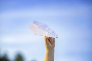 el Niños mano sostiene un blanco papel avión en contra el cielo. foto