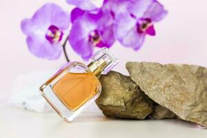 A perfume bottle stands on a stone against a background of beautiful orchids. Stylish appearance, layout, personality. Banner, a place for the text. photo