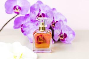 A perfume bottle on a pink background around beautiful orchid flowers. Stylish appearance, layout, personality. Banner, a place for the text. photo