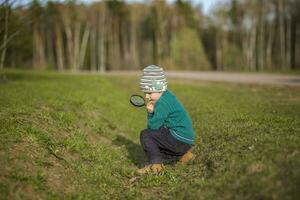 A funny boy walks through the spring park, examines the leaves with a large magnifying glass, looks for bugs and enjoys. photo