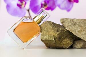 un perfume botella soportes en un Roca en contra un antecedentes de hermosa orquídeas. elegante apariencia, disposición, personalidad. bandera, un sitio para el texto. foto