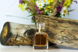 a perfume bottle on the background of a dry stump, tree bark and a bouquet of wild flowers. Stylish appearance, layout, personality. Banner, a place for the text. photo