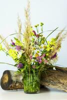 un seco tocón, árbol ladrar y un ramo de flores de salvaje flores en un pequeño vaso florero. elegante apariencia, disposición, personalidad. foto